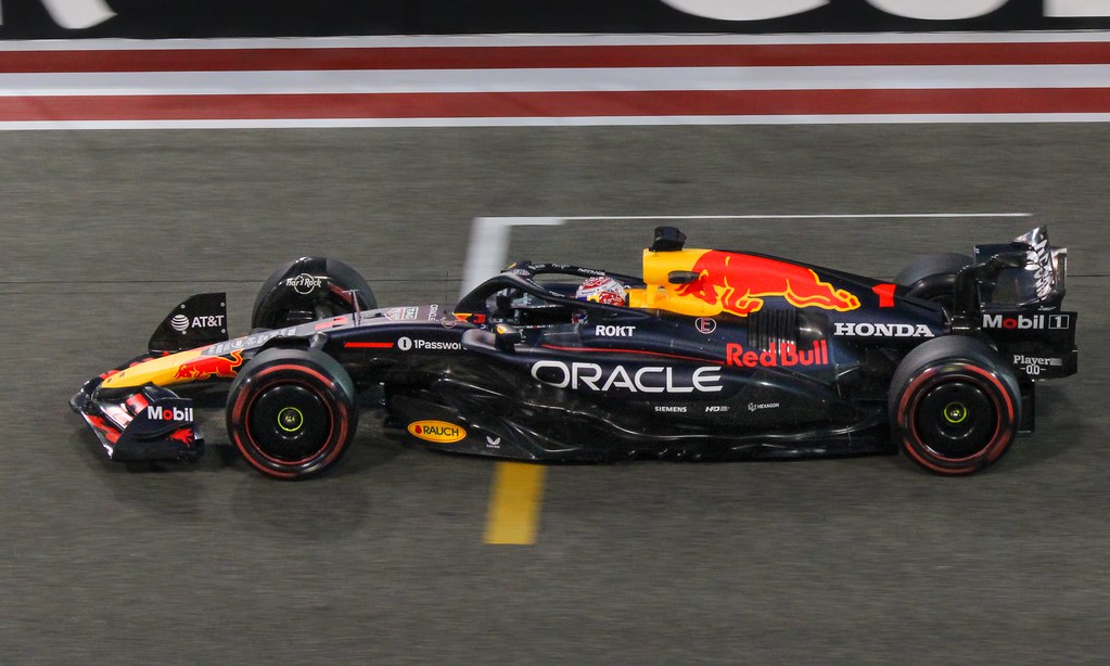 Max Verstappen mengendarai mobil Red Bull Racing di lintasan Grand Prix Spanyol 2025, dengan latar belakang aspal dan tribun penonton.